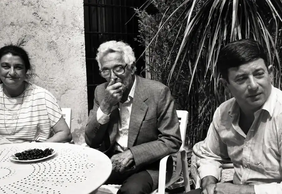 Photographie ancienne en noir et blanc de trois personnes réunies autour d’une table en extérieur