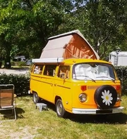 Combi Volkswagen jaune au toit relevable, stationné dans un cadre arboré.