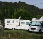 Deux camping-cars blancs stationnés près d’un espace végétalisé et d’une colline.