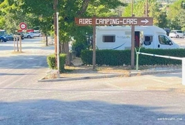 Panneau directionnel indiquant une aire de camping-cars, avec un véhicule stationné derrière une haie.
