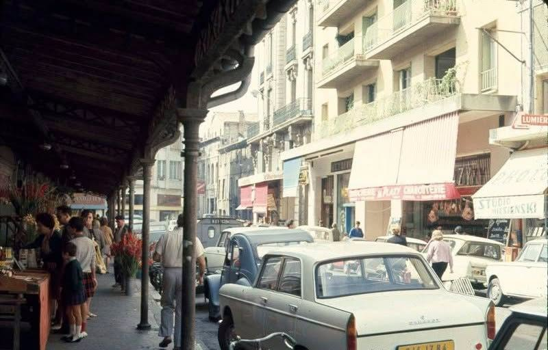 Anciennes Halles d'Avignon rue de la Petite-Meuse avant 1972, avec marquise métallique, étals de fleurs, passants, voitures anciennes et commerces.
