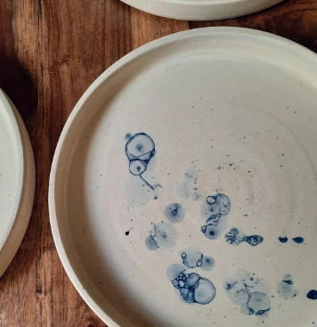 Assiettes en céramique claire d’Altésana, avec des motifs bleus, posées sur une table en bois.