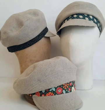 Trois chapeaux beiges de l’Atelier Ciboulette, ornés de bandes à motifs et présentés sur des supports.