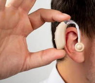 Gros plan d’une aide auditive placée derrière une oreille, tenue par une main.
