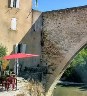 Terrasse avec un parasol rouge près d’une maison et de l’arche en pierre du Pont Roman de Nyons.