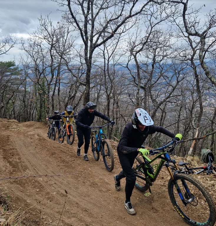 Quatre vététistes casqués poussent leurs vélos sur une piste en terre dans les bois du Bike Park de Nyons.