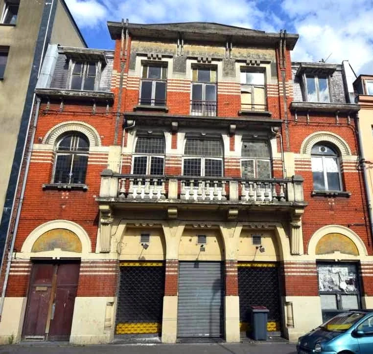 Façade de l'ancien cinéma Le Mondial au 90 rue Racine à Lille, avec ses briques rouges, ses bandeaux de pierre, son balcon et ses décors architecturaux.