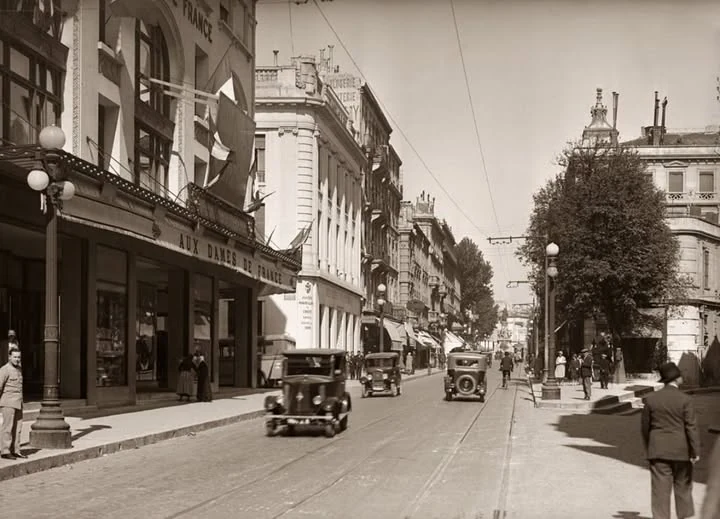 Rue de la République à Avignon autrefois, avec le magasin Aux Dames de France, des automobiles et les rails du tramway.