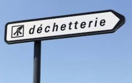 Panneau blanc indiquant la direction de la déchetterie sur fond de ciel bleu.