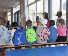 Enfants portant des cartables, assis sur un banc à l’intérieur d’une école.