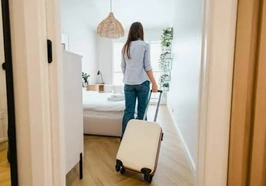 Une personne avec une valise à l’entrée d’une chambre lumineuse.