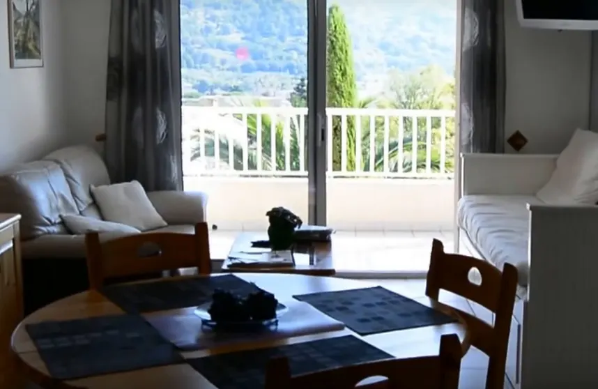 Salon avec fauteuils, table basse et baie vitrée ouverte vers une terrasse.