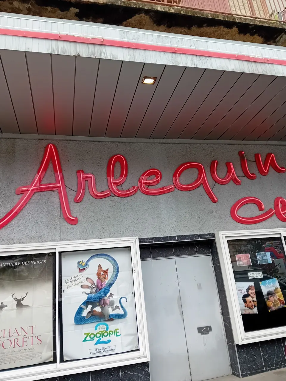 Photographie verticale de l’enseigne et des affiches du cinéma L’Arlequin à Nyons.