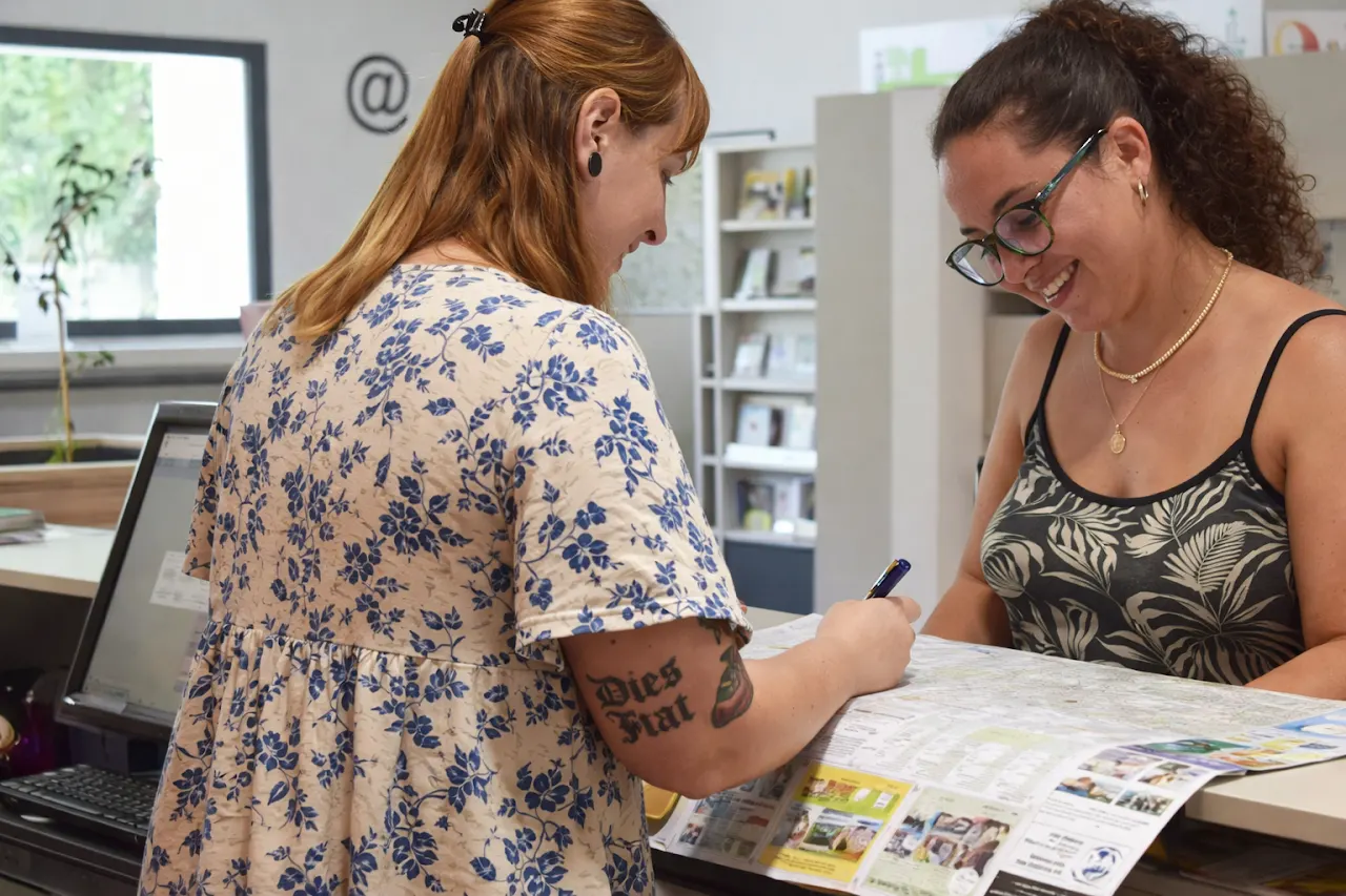 Accueil à l’Office de Tourisme de Nyons, deux personnes échangent autour d’un plan et de brochures pour organiser leurs visites.