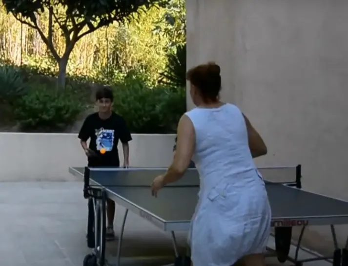 Deux personnes jouant au tennis de table dans un espace extérieur arboré.