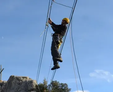 Personne équipée de via ferrata traversant des câbles suspendus au-dessus d’un rocher