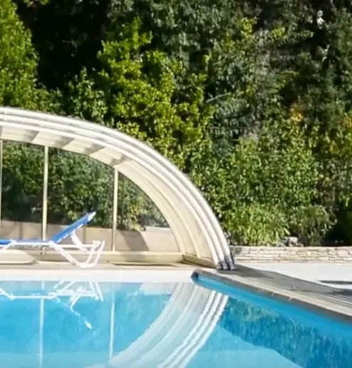 Piscine avec abri arrondi ouvert et transats au bord du bassin.