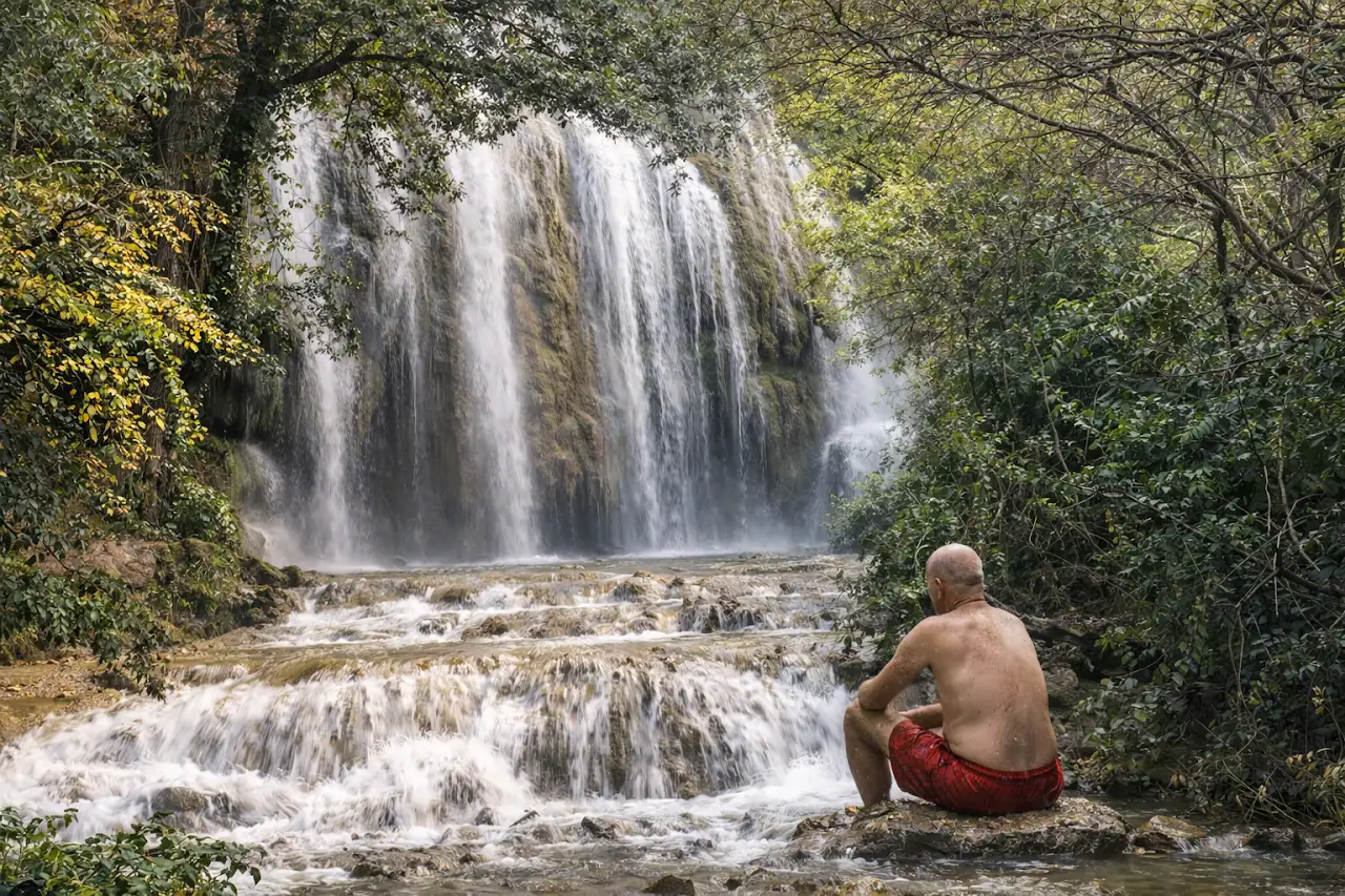 Moment de calme à la cascade d’Aubres, homme assis au bord des chutes d’eau.