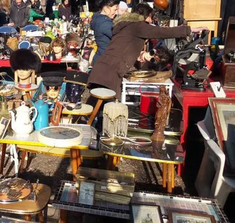 Visiteurs parmi des stands de brocante chargés de vaisselle, jouets et objets de seconde main