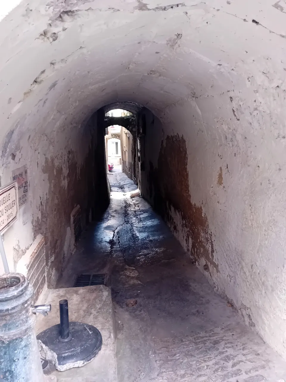 Passage voûté étroit dans le vieux Nyons, ruelle ancienne en pierre reliant deux rues, avec sol pavé et lumière naturelle au fond, en Drôme provençale.