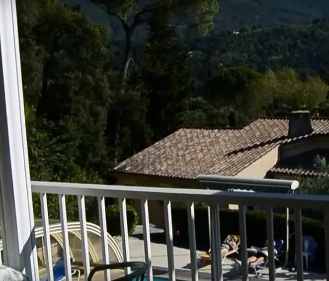 Balustrade de terrasse donnant sur les toits, les arbres et la piscine.
