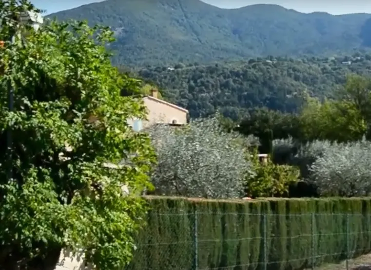 Jardin et végétation avec une maison et les montagnes à l’arrière-plan.