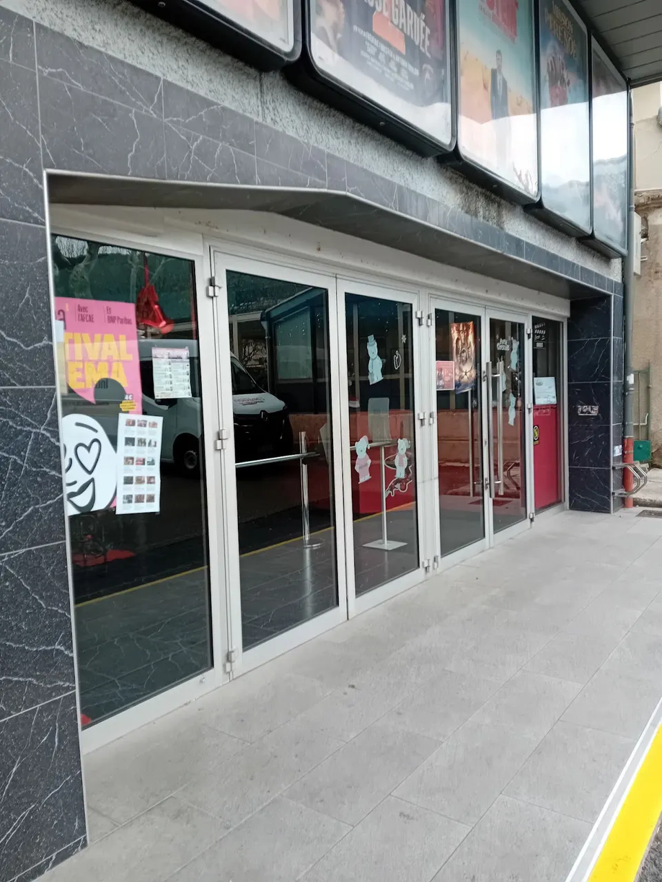Entrée vitrée du cinéma L’Arlequin à Nyons, entourée d’affiches de films.