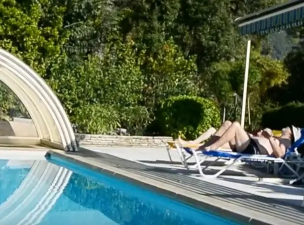 Piscine et transats avec une personne allongée à côté de l’abri ouvert.
