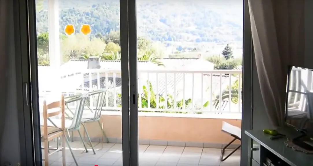 Baie vitrée ouverte sur une terrasse avec table, chaises et vue vers les montagnes.