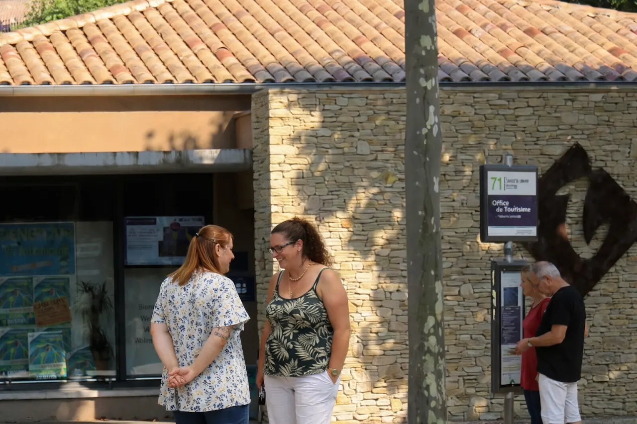 Devant l’Office de Tourisme de Nyons, plusieurs visiteurs consultent les panneaux d’informations et échangent sur la place centrale, à deux pas du marché.