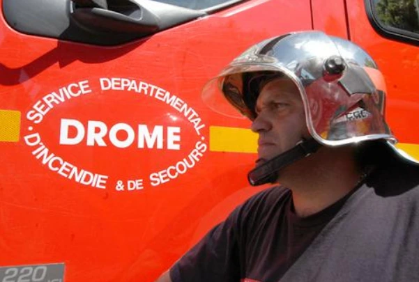 Un sapeur-pompier casqué devant un véhicule rouge portant l’inscription SDIS Drôme.