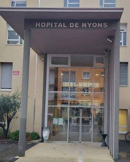 Entrée de l’hôpital de Nyons, avec portes vitrées et enseigne sous un auvent.
