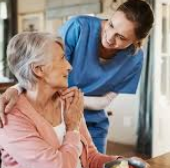 Professionnel de santé en tenue bleue échangeant avec une femme âgée assise.