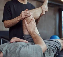 Un professionnel soutient la jambe fléchie d’un patient allongé pour mobiliser son genou.