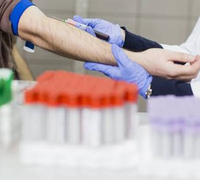 Prélèvement sanguin au pli du coude par une professionnelle portant des gants, avec des tubes au premier plan.