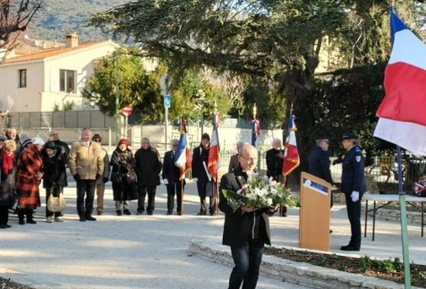 Cérémonie commémorative avec une gerbe de fleurs, des porte-drapeaux et des habitants réunis