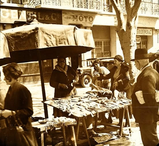 Marché du Prado à Marseille en 1931, avec des femmes autour d'un étal de poissons sur tréteaux, un homme en costume et chapeau, et une automobile en arrière-plan.