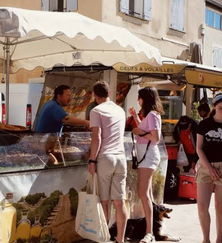 Des visiteurs devant un étal de produits alimentaires sous les parasols du marché.