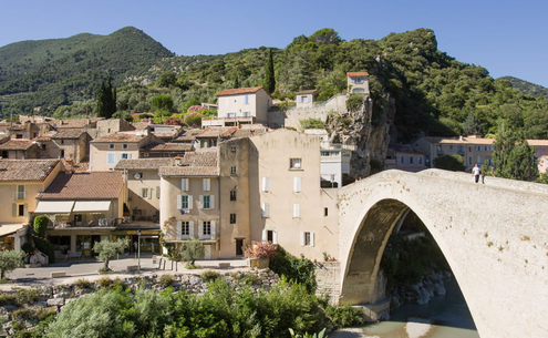 Le Pont Roman de Nyons, les maisons au bord de l’Eygues et les collines sous un ciel bleu.