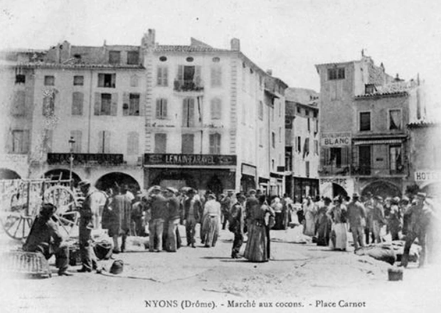 Carte postale du marché aux cocons de Nyons, place Carnot, avec des vendeurs et des acheteurs devant les arcades.