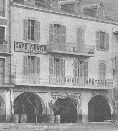 Ancienne façade sous les arcades de Nyons, avec une enseigne Librairie Papeterie et celle d’un café à l’étage.