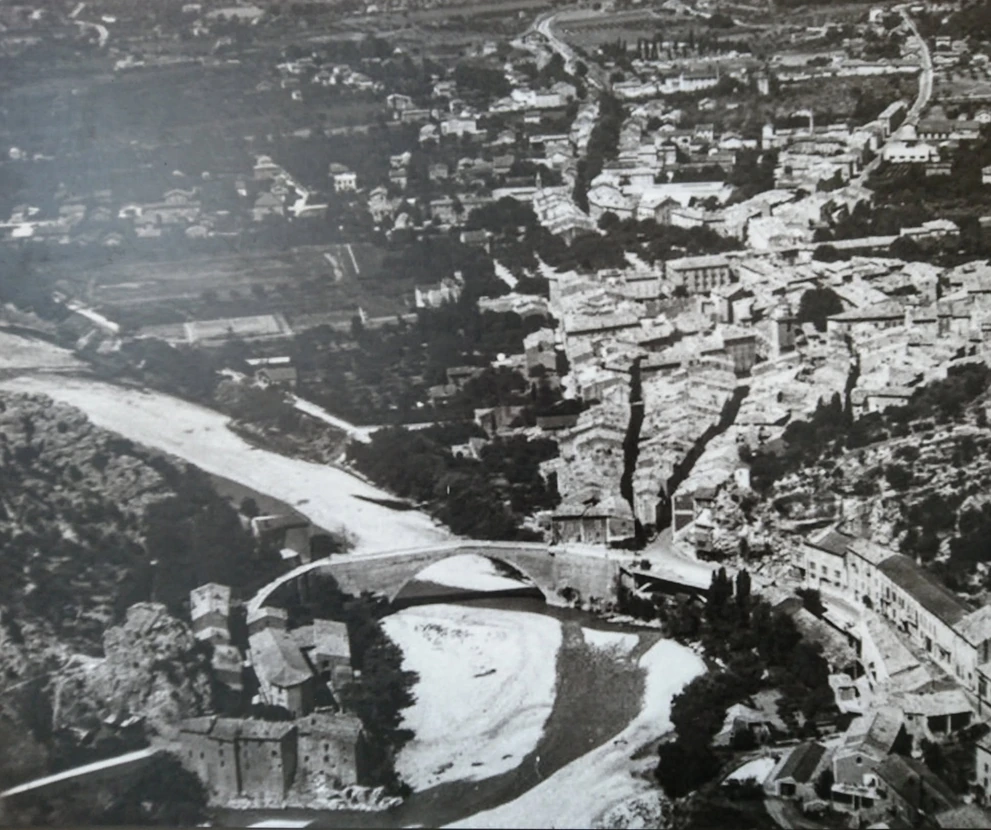 Vue plongeante ancienne de Nyons vers 1900 : pont Roman sur l’Eygues et rues des Bas-Bourgs et des Déportés formant un V entre les maisons.