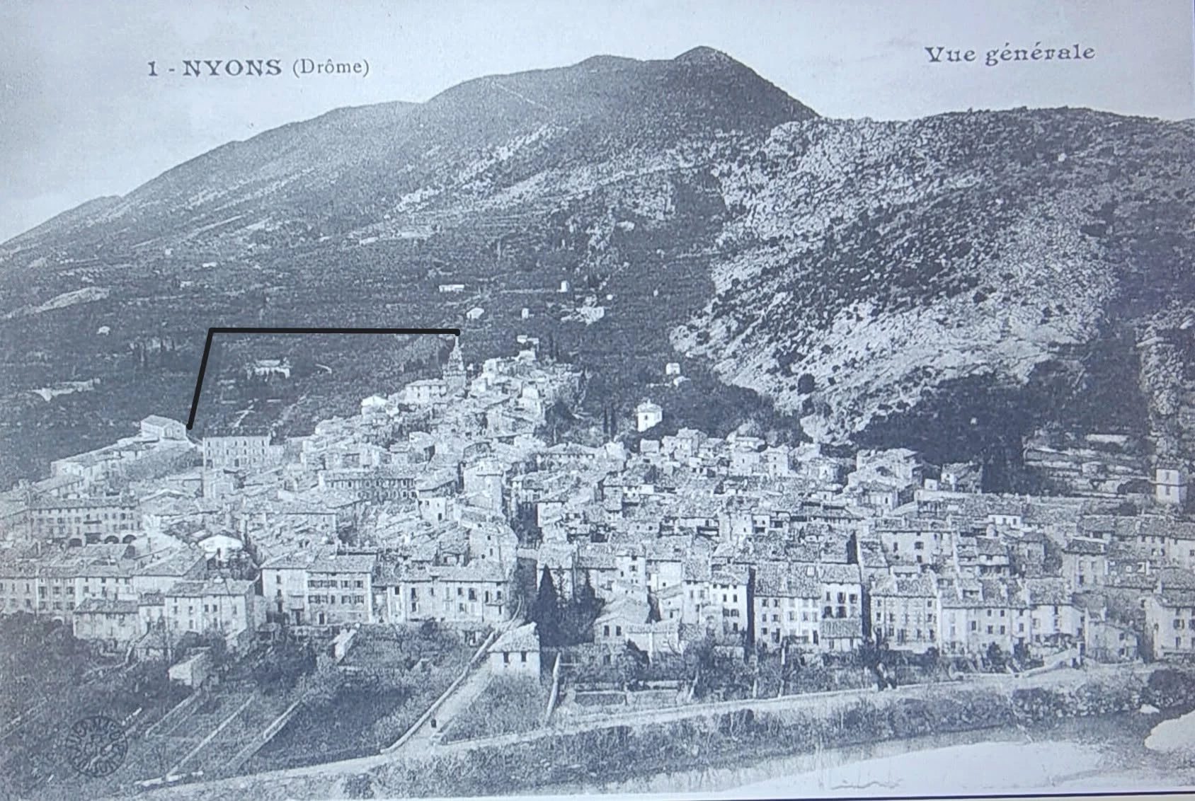 Carte postale ancienne montrant une vue générale de Nyons sous les montagnes, avec une annotation noire sur la partie gauche.