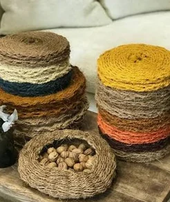 Scourtins en fibre végétale empilés, de différentes couleurs, avec un panier de noix au premier plan.