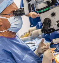 Professionnel en tenue opératoire utilisant un microscope lors d’une intervention sur l’œil.