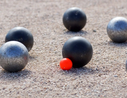 Boules de pétanque sur un terrain de gravier, près d’un cochonnet rouge.