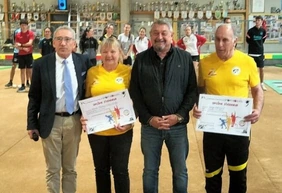 Remise de diplômes dans un boulodrome, devant une collection de trophées.