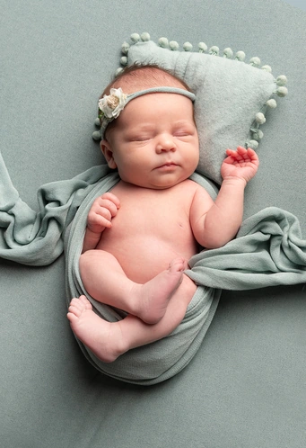 Nouveau-né endormi, enveloppé dans un tissu vert sauge, avec un bandeau fleuri.