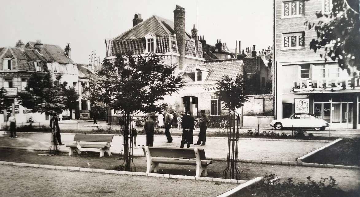 Ancienne place de la République à Rosendaël, aujourd'hui place de l'Europe, avec ses bancs, le cinéma Le Régent, une Citroën DS et des habitants près du terrain de boules.