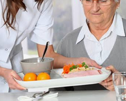 Un plateau-repas avec des fruits et un plat est présenté à un homme âgé assis à table.